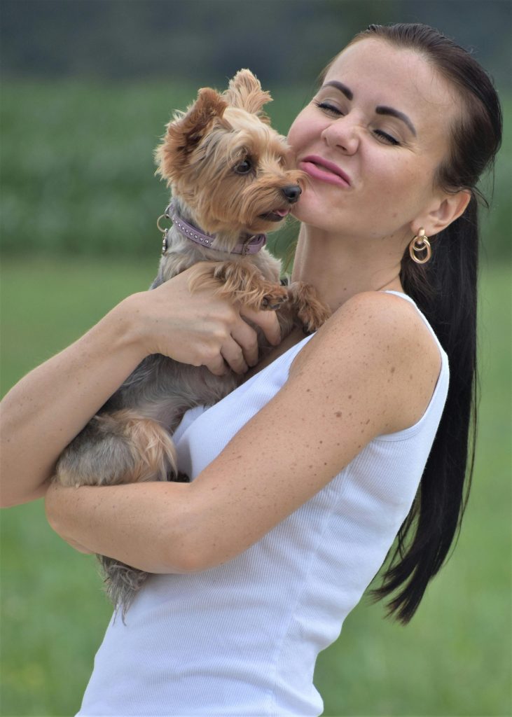 Smiling woman cuddling her Yorkshire Terrier outdoors, radiating happiness.